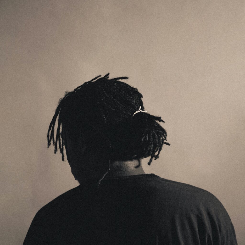 Back view portrait in sepia tone of a man with dreadlocks wearing a black shirt in a studio setting.